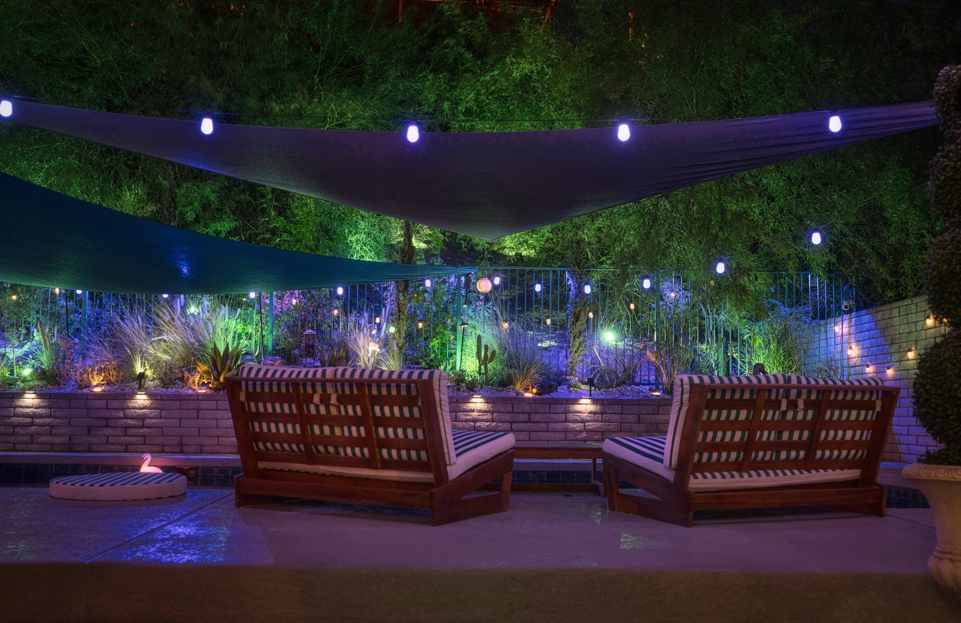 Rear view of teak lounge chairs in a desert oasis yard at night, overlooking a mountain lit by magical outdoor lighting. Peaceful, stylish, and glowing with warmth.