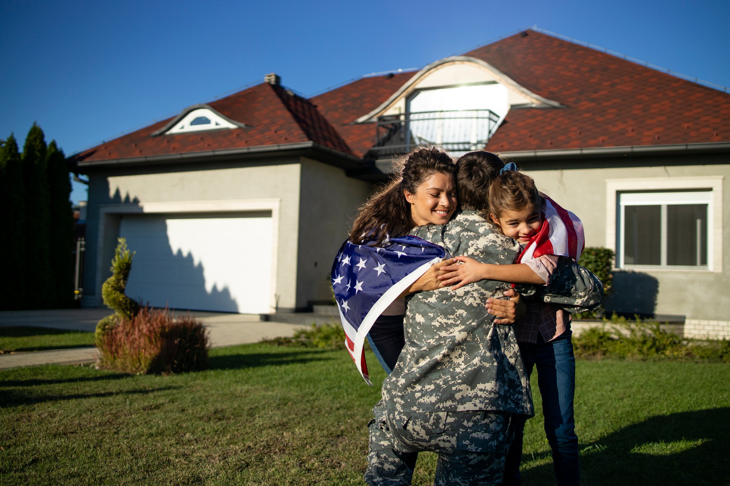 Soldier in uniform coming home and his lovely family with American flag running into his arms celebrating reunion.