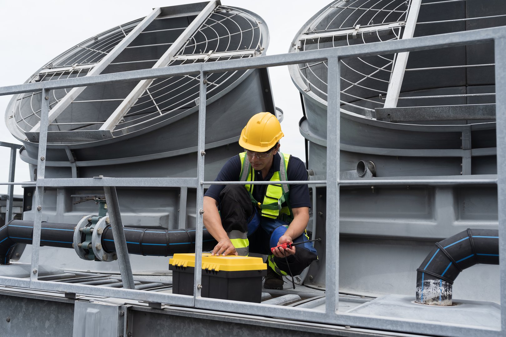 Cooling tower on rooftop. Induced draft cooling tower. Male engineer or technician maintenance and repair of cooling tower on rooftop of building, wearing safety uniform, helmet, using handyman tools