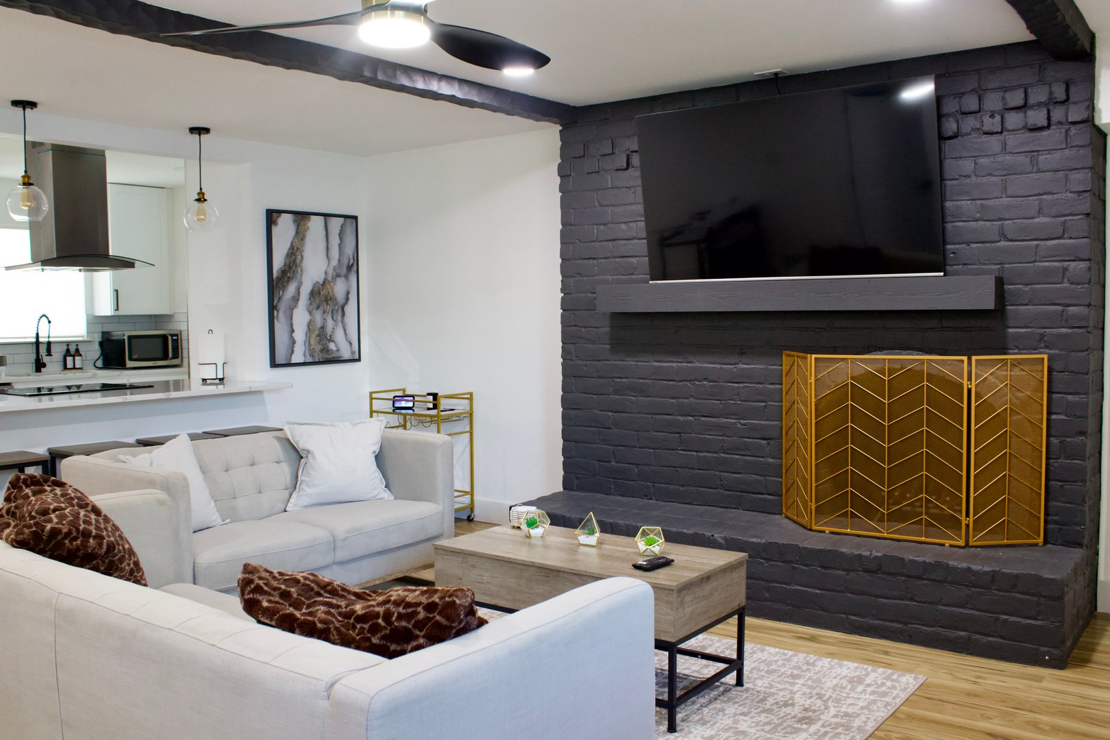 Modern living room with gray sofas, a wall-mounted TV above a black brick fireplace, and a wooden coffee table.