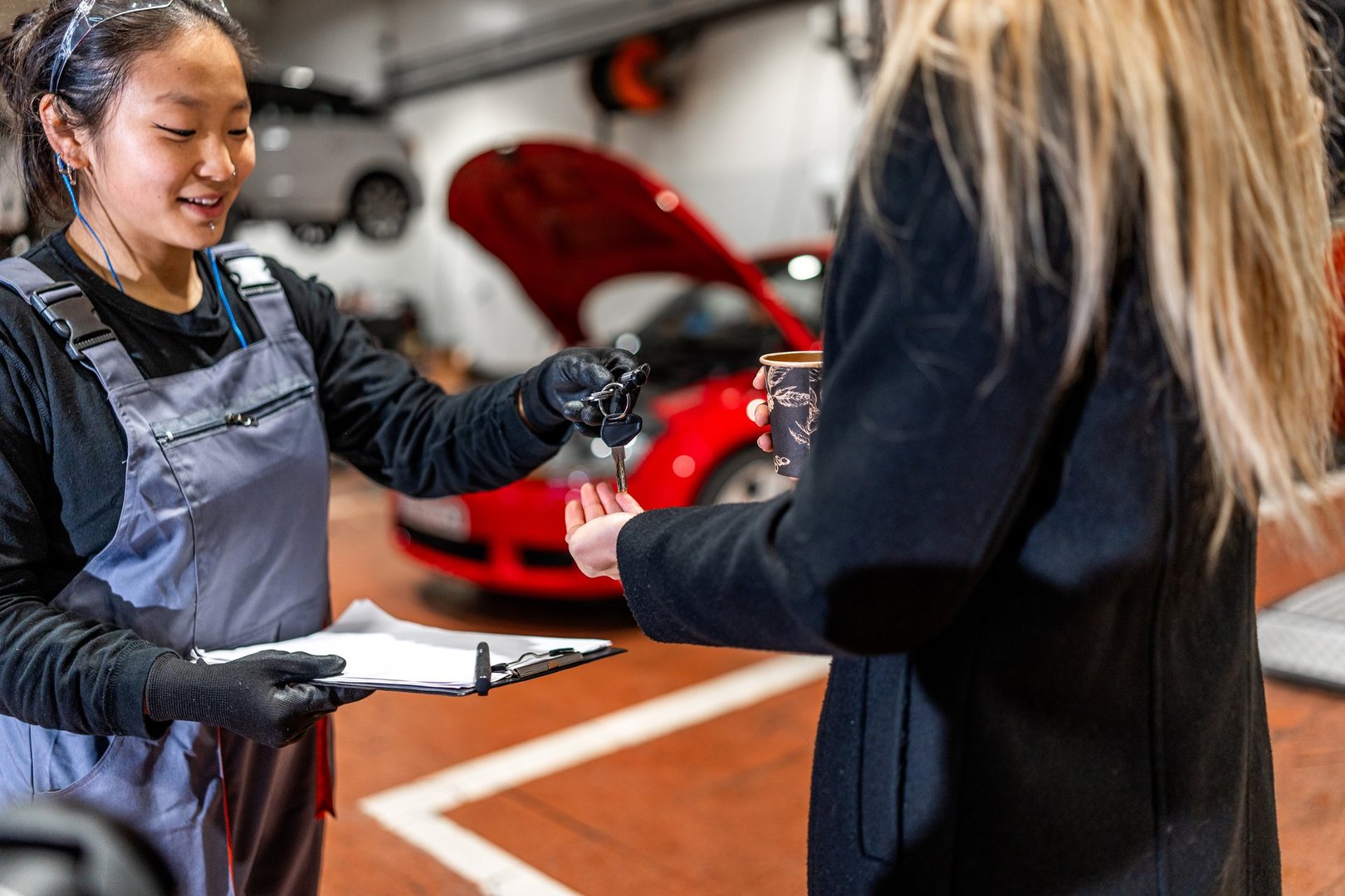 Professional female mechanic handing over car keys to a customer after completing maintenance in a car workshop