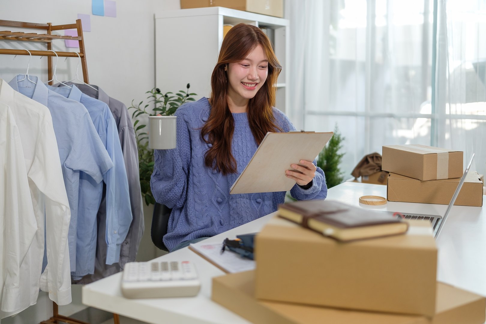 Small business owner reviewing orders and drinking coffee in a home office. E-commerce and online business concept.