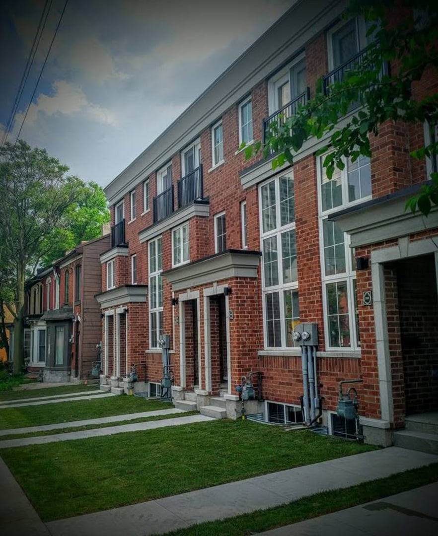 Row of modern brick townhouses with large windows, small lawns, and clear sky overhead.