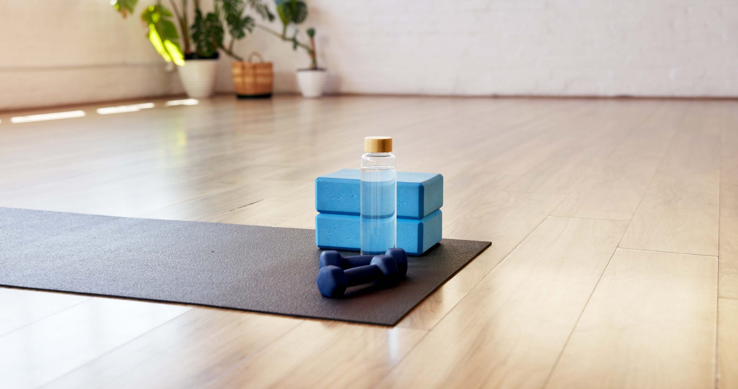 Yoga, water and block with dumbbells in studio for fitness, empty room and wellness class. Pilates session, electrolyte bottle and interior of health club for training weights, holistic and gym
