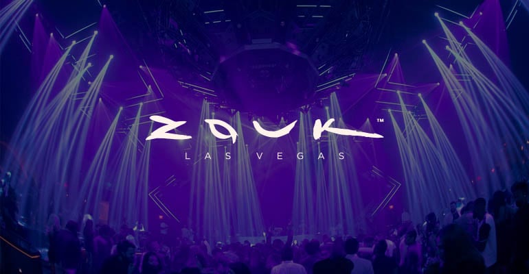 A vibrant nightclub scene with purple lighting beams and the text "Zouk Las Vegas" in white on a crowded dance floor.