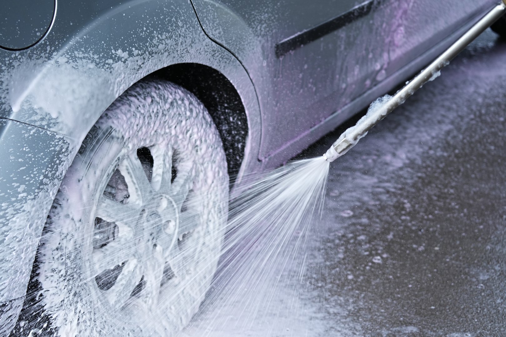 The moment of car washing, where active foam is applied to the wheel and part of the body from a foam generator connected to a high-pressure device.