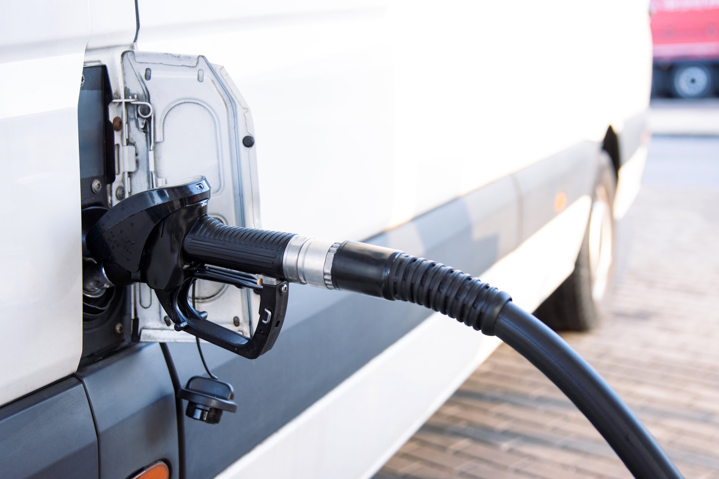 Closeup of a fuel nozzle in the car tank. Process of refilling a white transporter bus at a gas station. Refueling pistol inserted into a vehicle at a gas station. Copy space