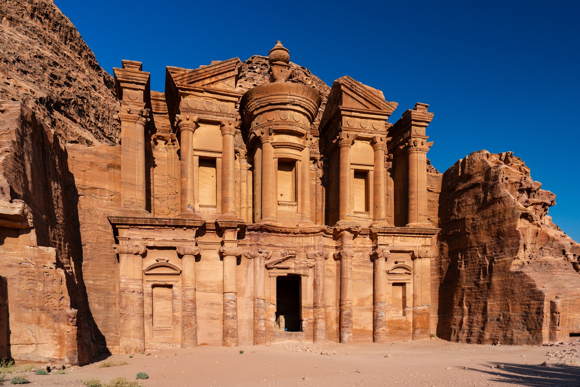 Impressive view of the ancient Al-Deir Monastery carved into the sandstone cliffs in Petra, Jordan, under a clear blue sky.