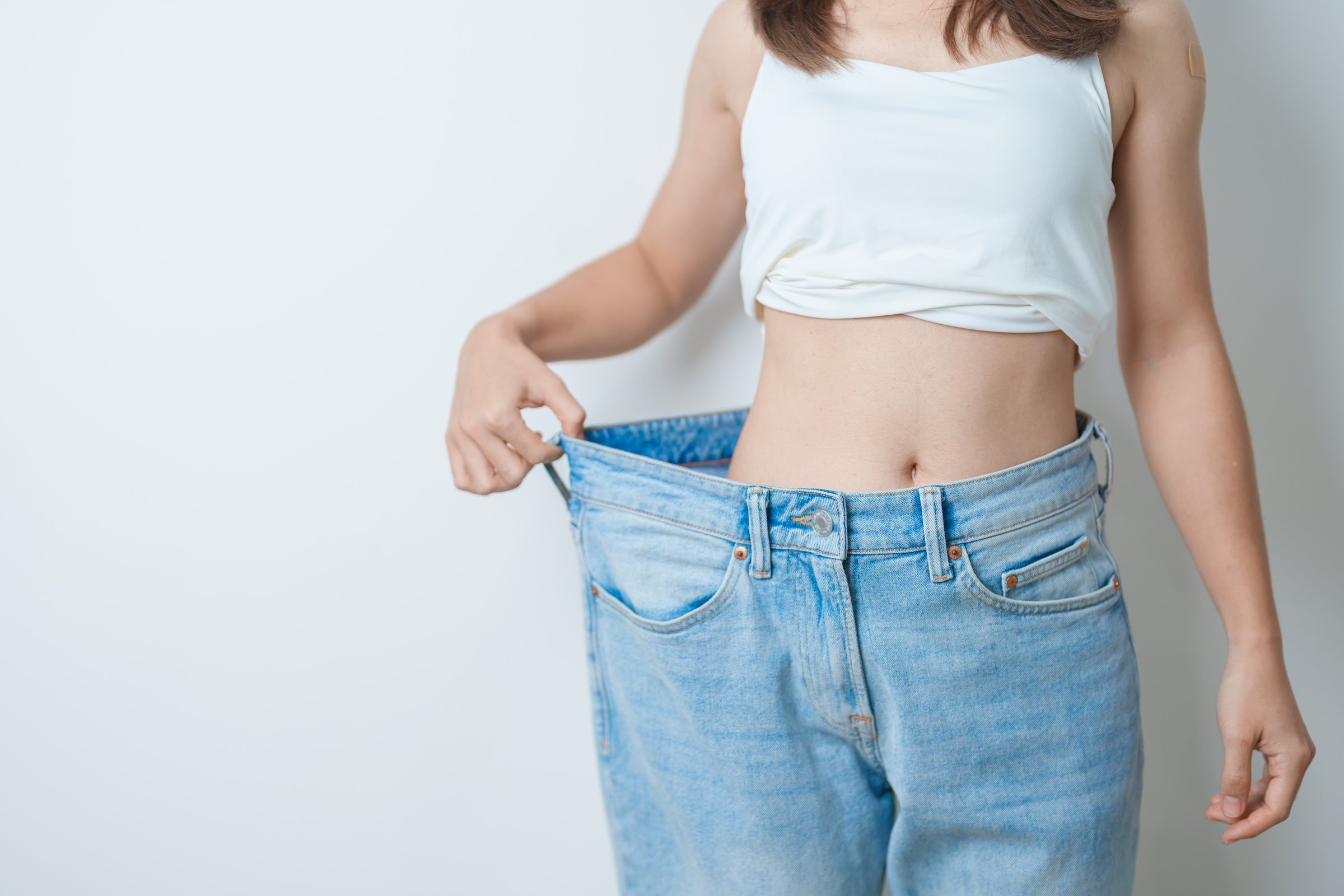 young slim female wearing big or oversize jeans, woman show healthy shape after weight loss. dieting, exercise, body fit and liposuction surgery concept
