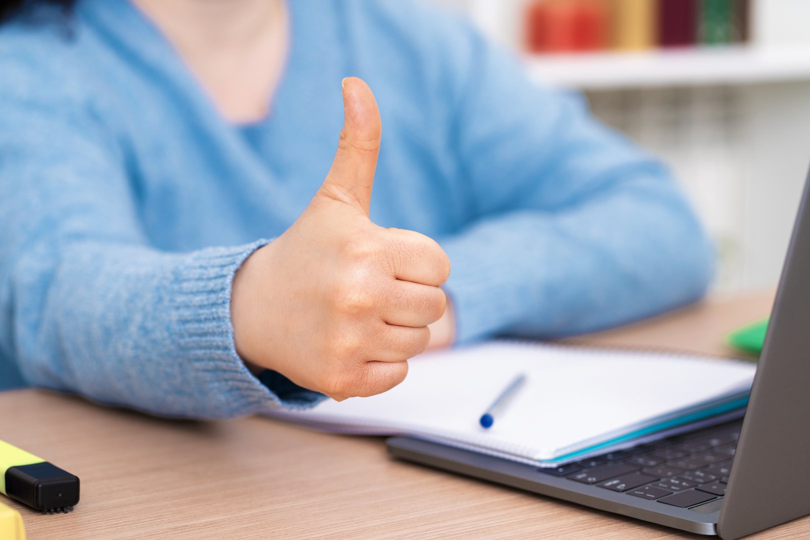 Close up of girl hands gesturing thumbs up using laptop on a desk at home