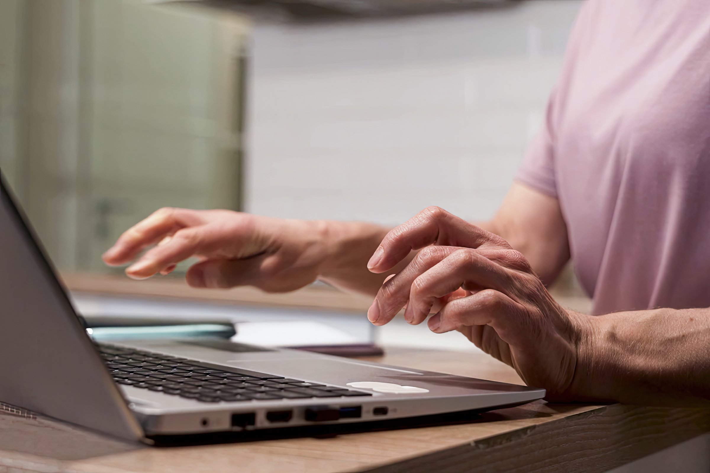 Close-up of elderly woman typing on laptop on kitchen table while studying online