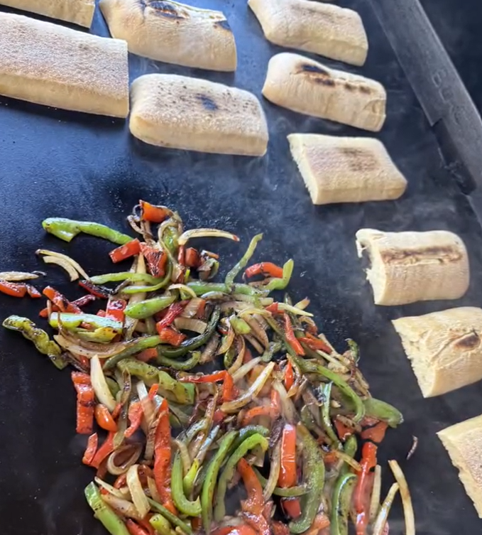 Toasting rolls and finishing peppers and onions on flattop