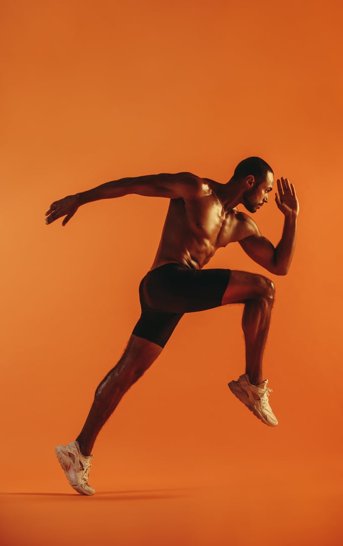 Bare chested athlete running with big stride forward on orange background. African american sportsman sprinting.