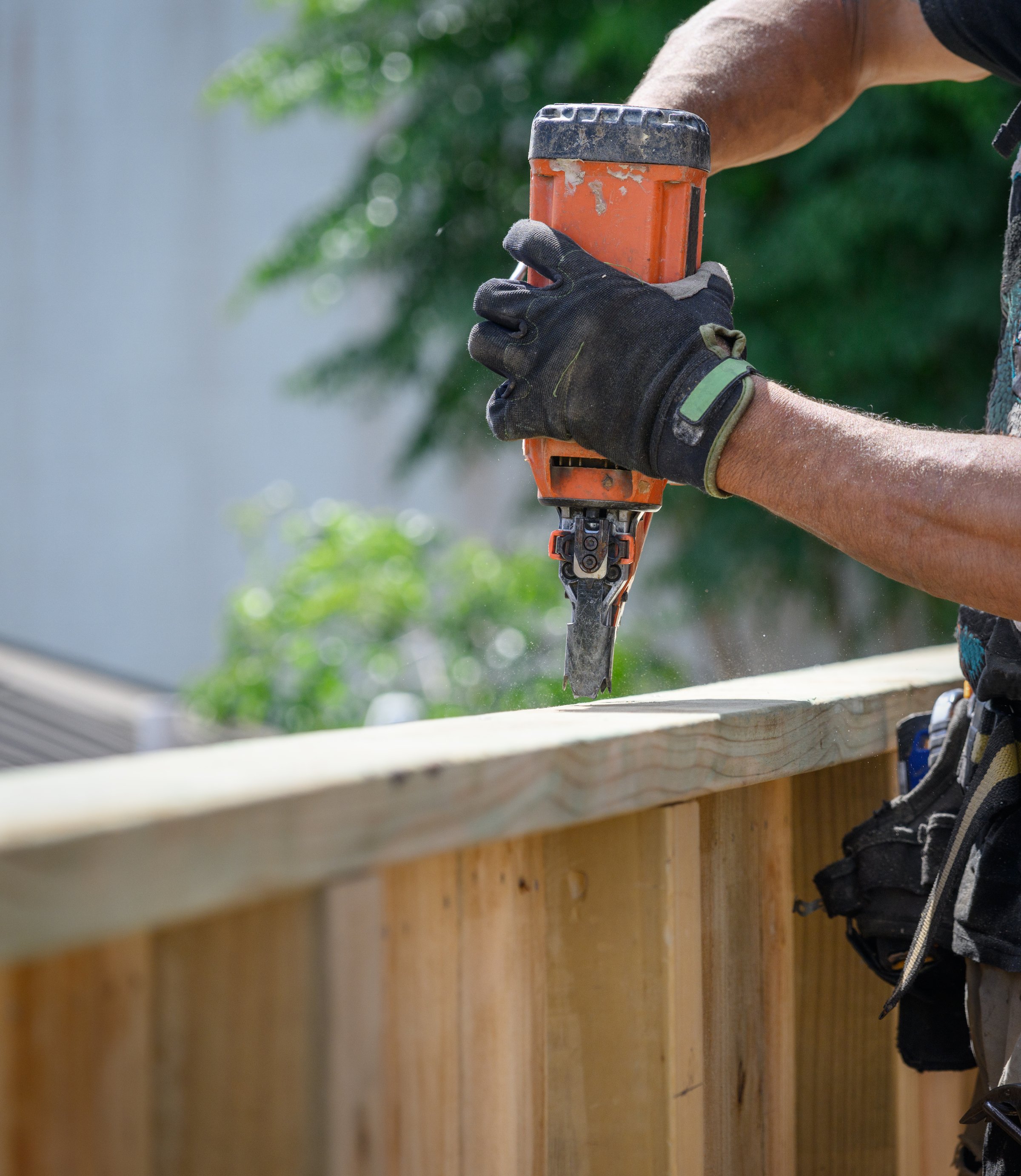 Hands of a professionally equipped builder working on fence using a nail gun construction tool.