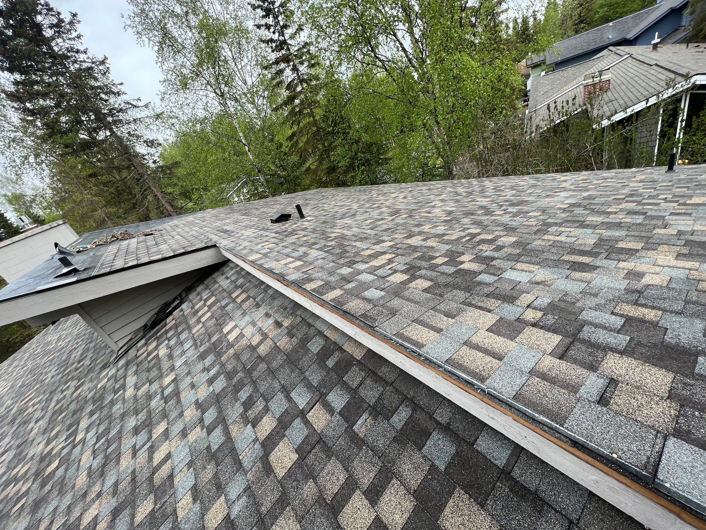 Residential roofing Anchorage Alaska - newly installed shingles on sloped roof surrounded by trees showcasing quality roof installation