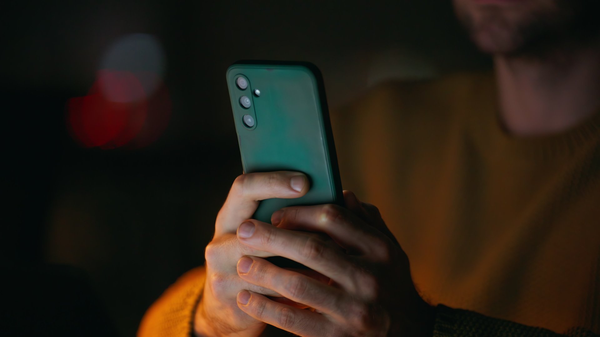 Startuper hands holding cellphone in night remote office closeup. Unrecognizable man watching smartphone sitting dark apartment alone. Freelancer browsing online store on mobile phone at evening home.