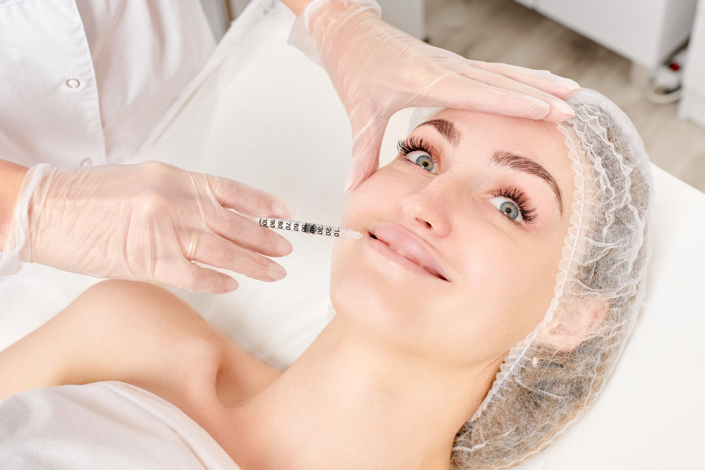 Cosmetologist makes fillers injection for lips augmentation and volume, non surgical cosmetic procedure in beauty salon. Beautician specialist hands in gloves makes treatment injection with syringe