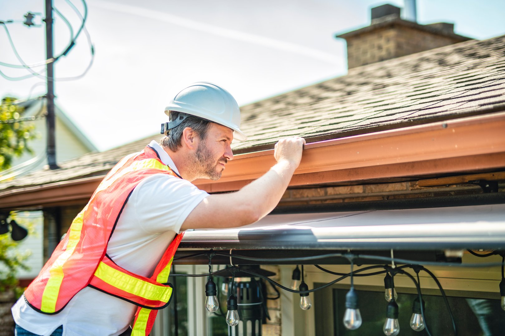 A man with hard hat standing on steps inspecting house roof