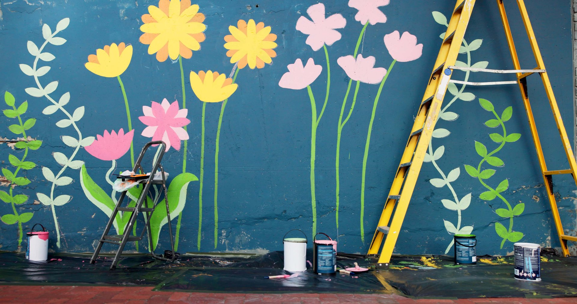 DIY, ladder and painting with mural on wall in street for decoration, improvement or renovation. Creative, background and flowers outdoor for community art project, design or neighborhood upliftment