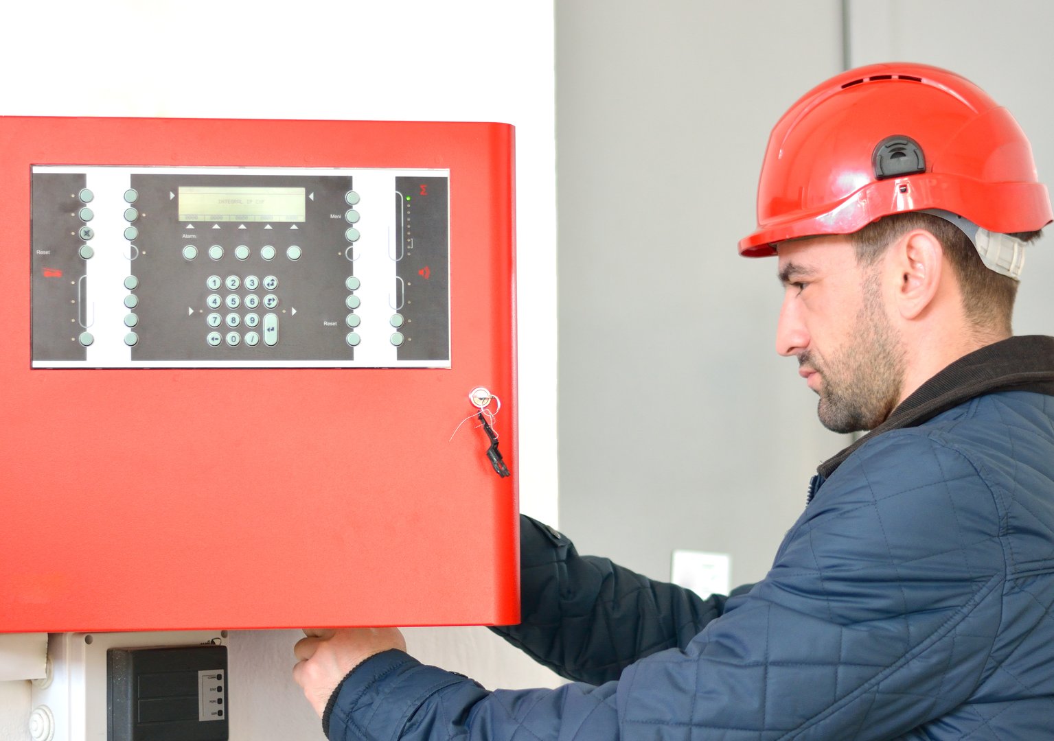 Young attractive electrical engineer at work with a red helmet on his head