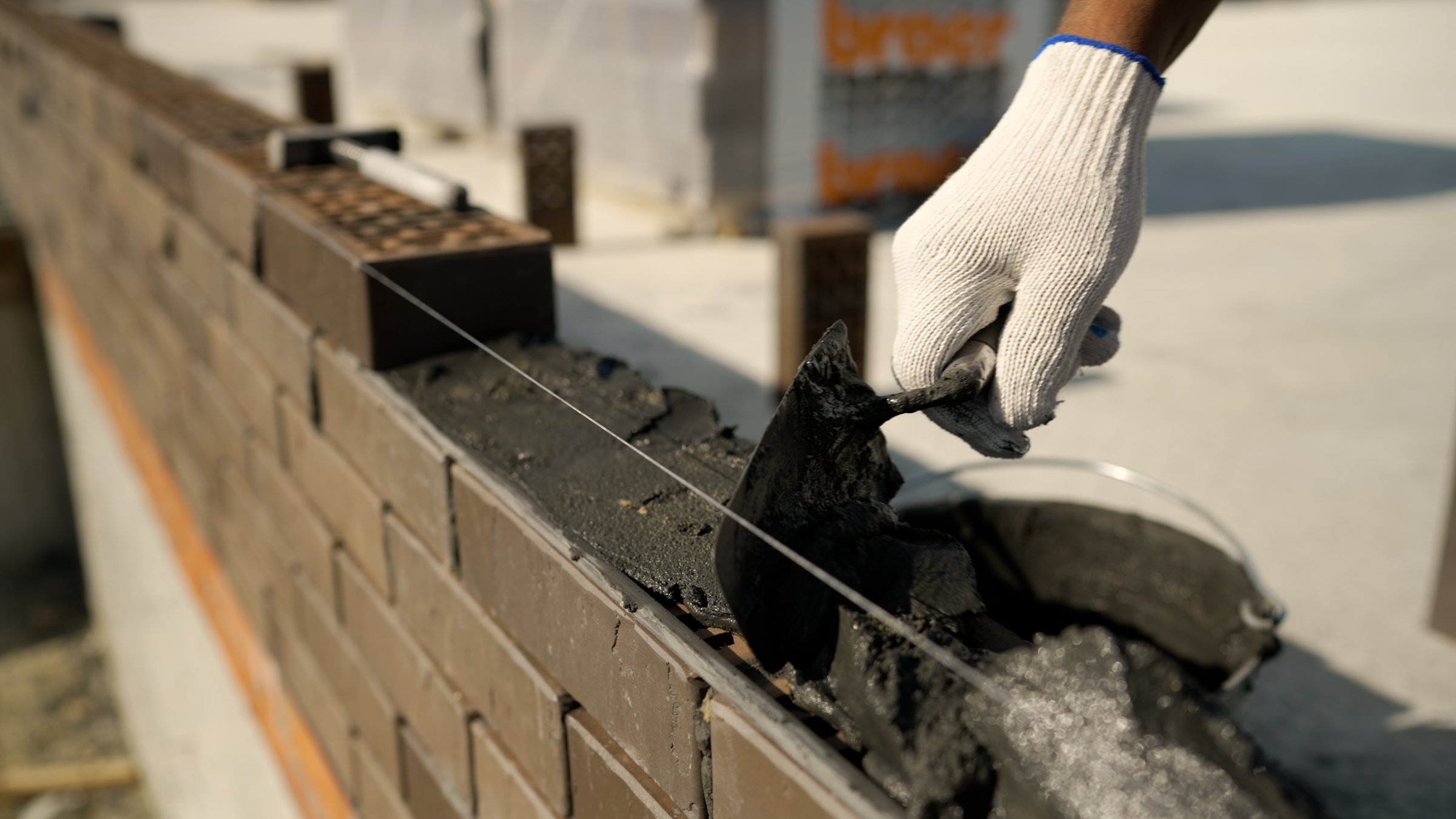 Skilled bricklayer carefully spreading mortar and precisely positioning bricks while constructing wall at active construction site, showcasing professional masonry techniques