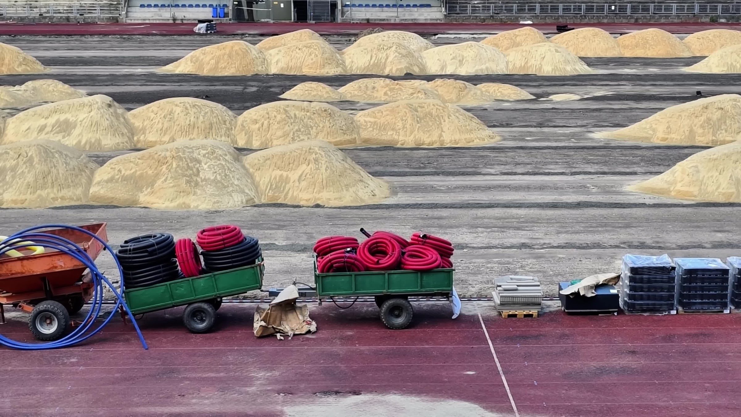 In a large industrial space, grain piles and equipment carts display the ongoing harvest activities
