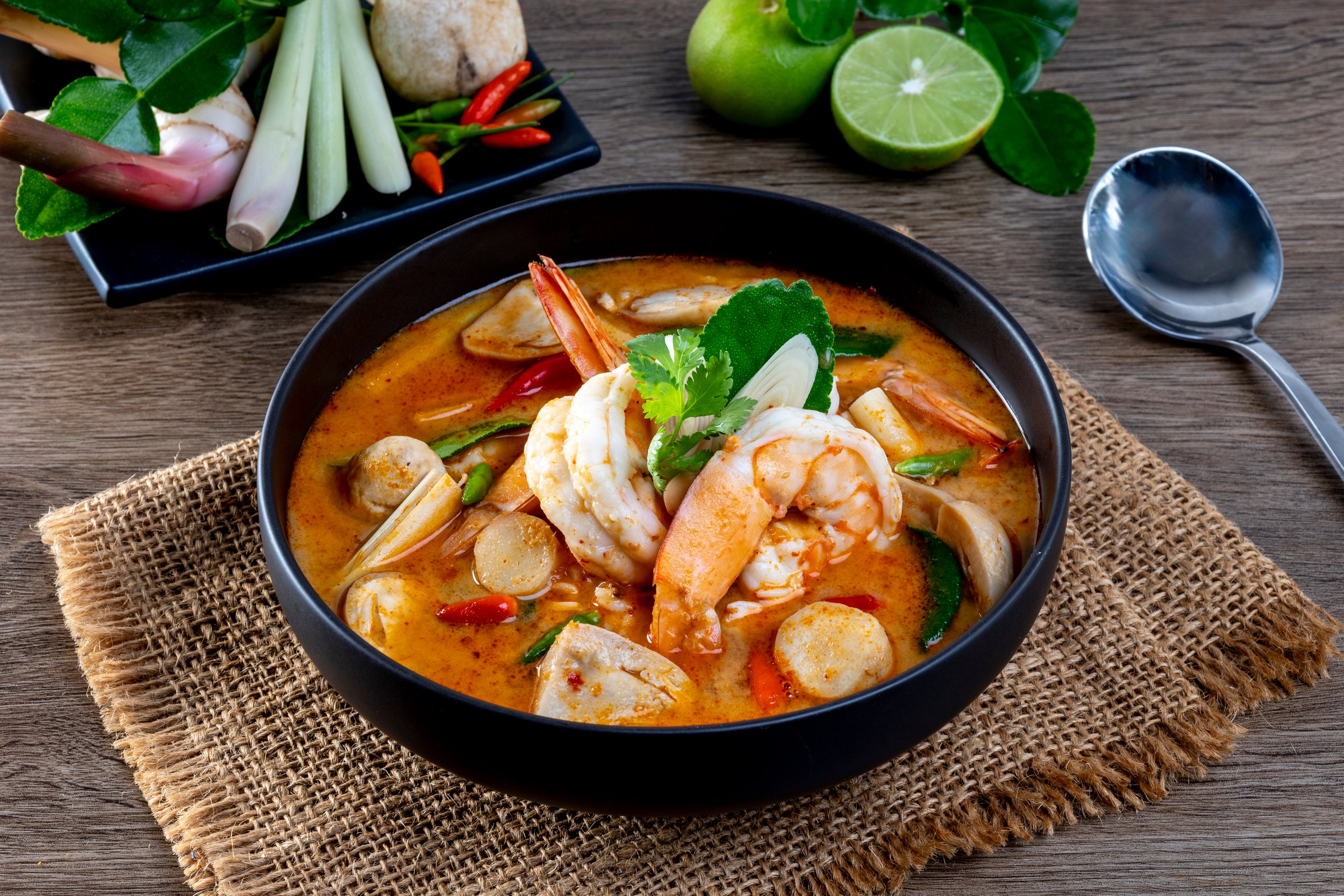 Prawn Tom Yum in a black bowl on a wooden table