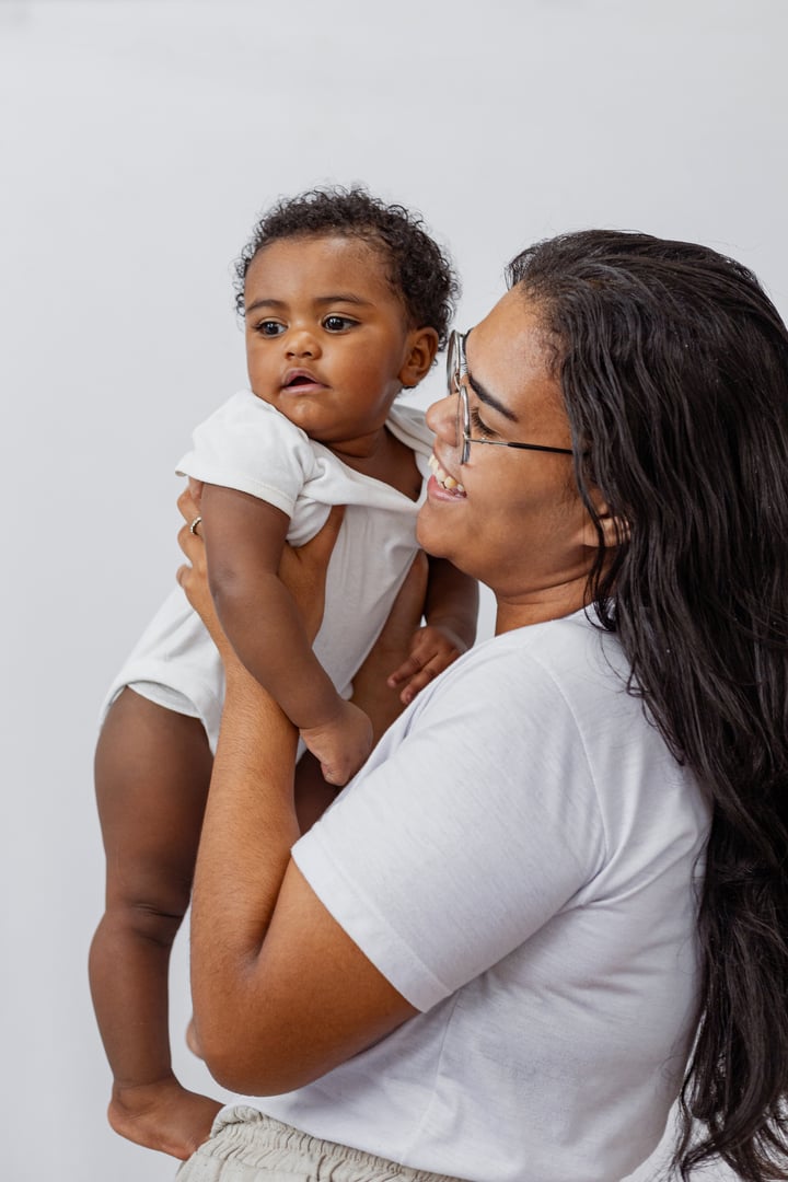 Beautiful Brazilian mother hugs and kisses her baby in the studio on a white background. A young mother in a white bodysuit hugs and plays with her baby in the studio. Black baby, African baby. Brazil