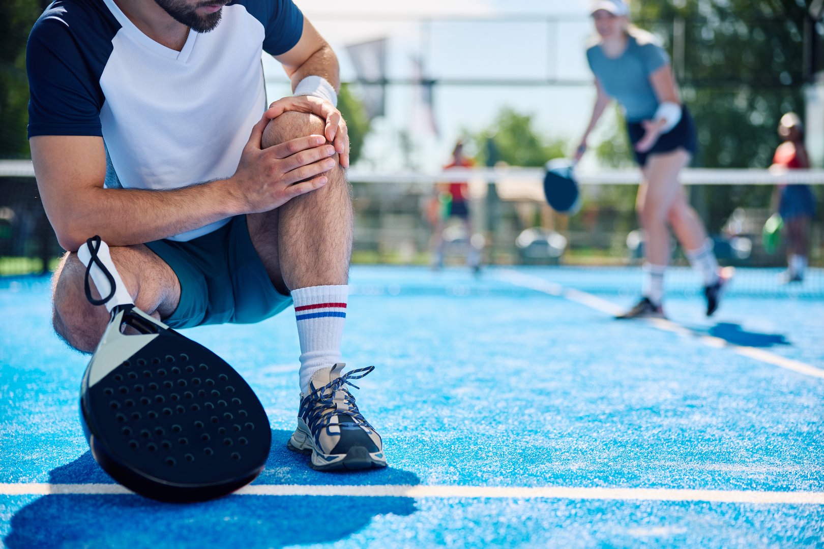 Close up of paddle tennis player holding his injured knee during mixed doubles match. Copy space.