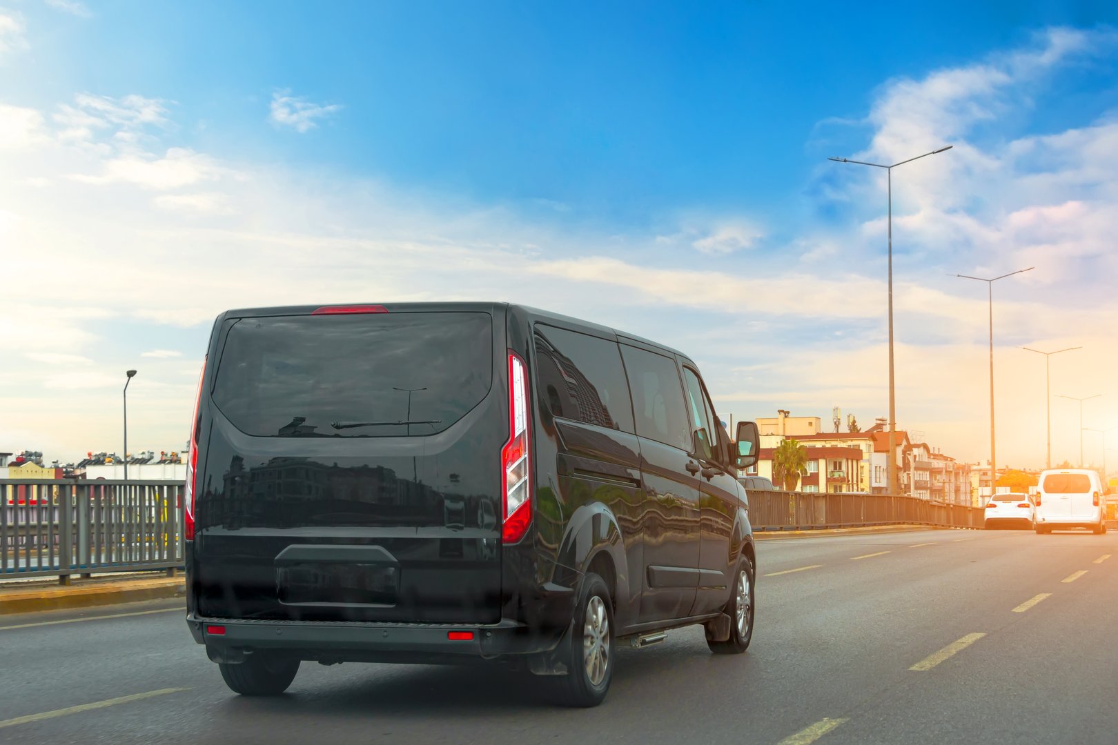 Black modern passenger charter van with a small delivery moves fast on the highway to the urban suburbs. Business distribution and logistics express service. Mini bus rides along the highway