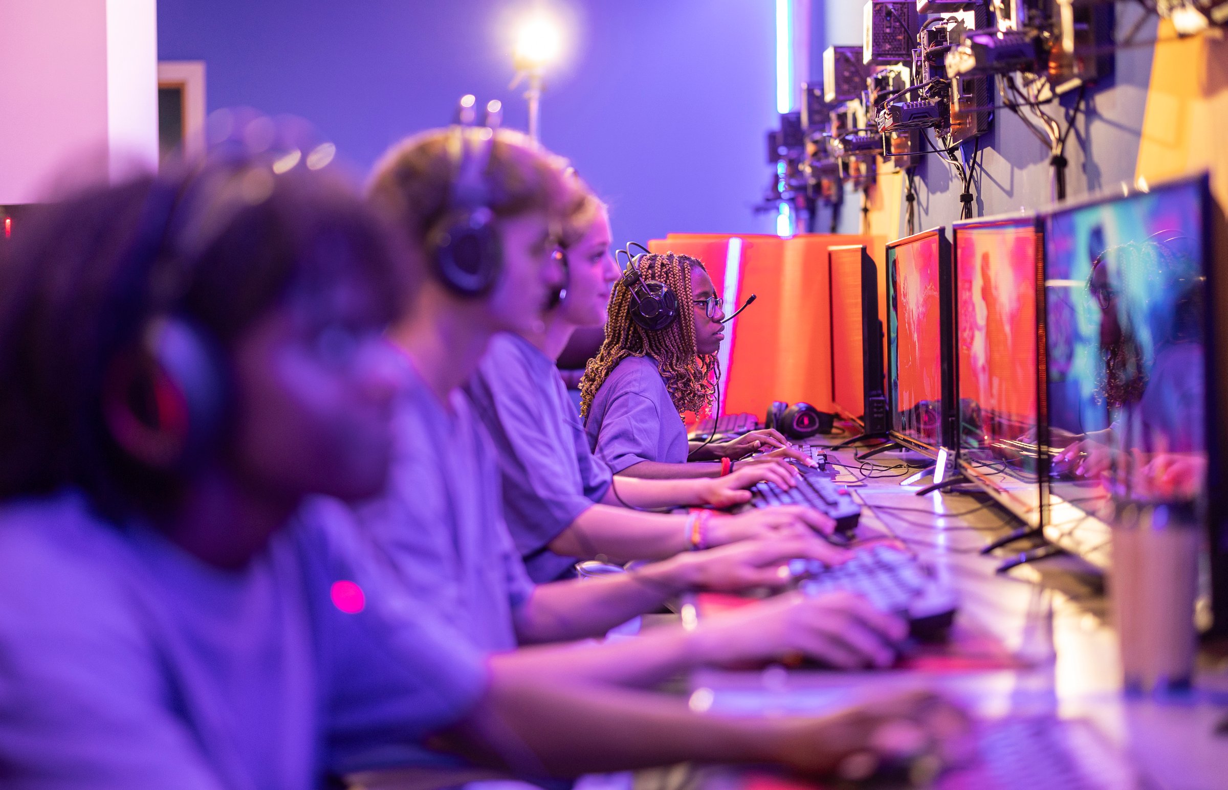 Team of professional e-sports players playing video games at cyber gaming tournaments indoors - focus on african woman -