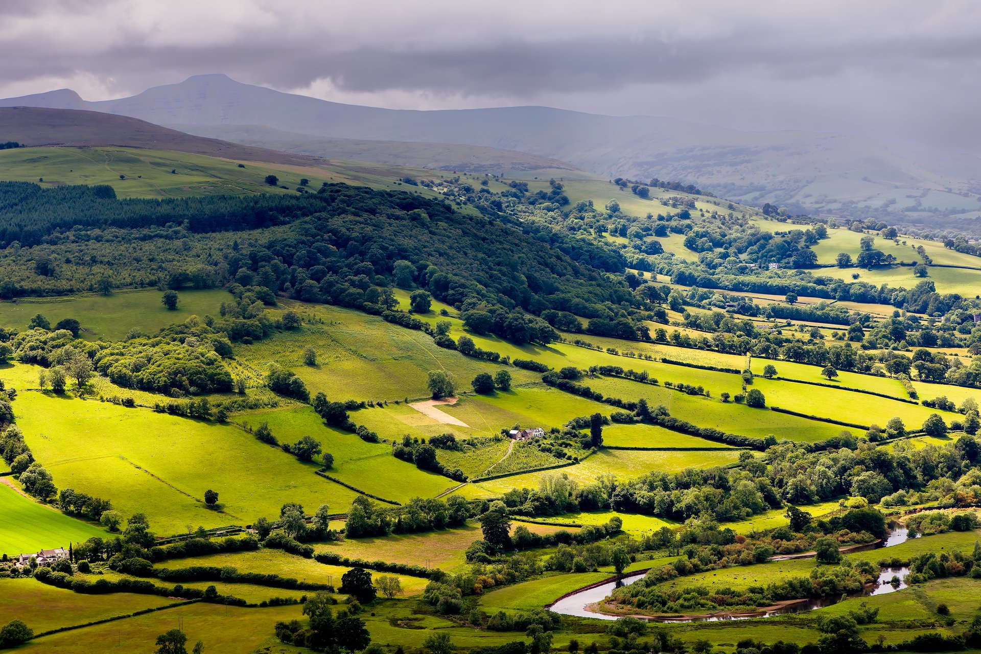 Rain falling over lush, green farmland and hills