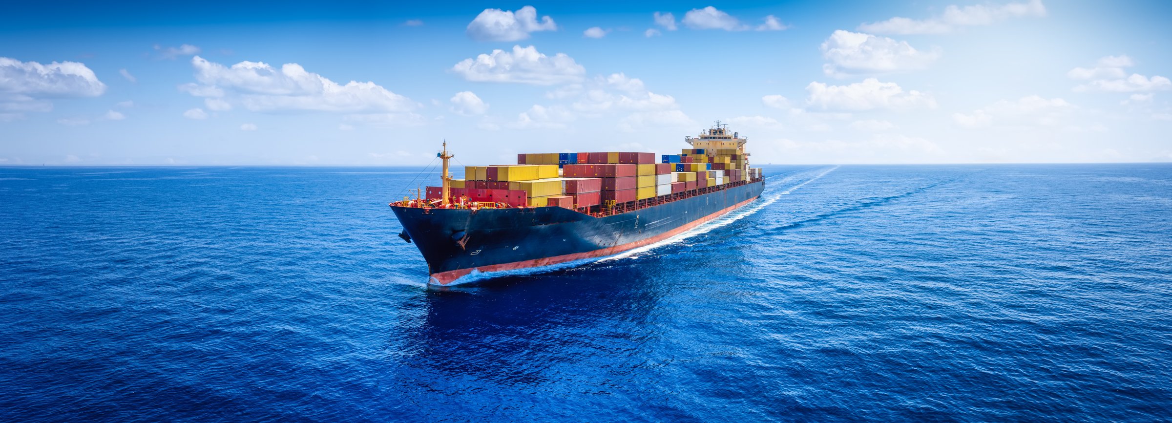 Panoramic aerial view of a loaded container cargo carrier ship sailing over the open ocean as a banner for transport and industry