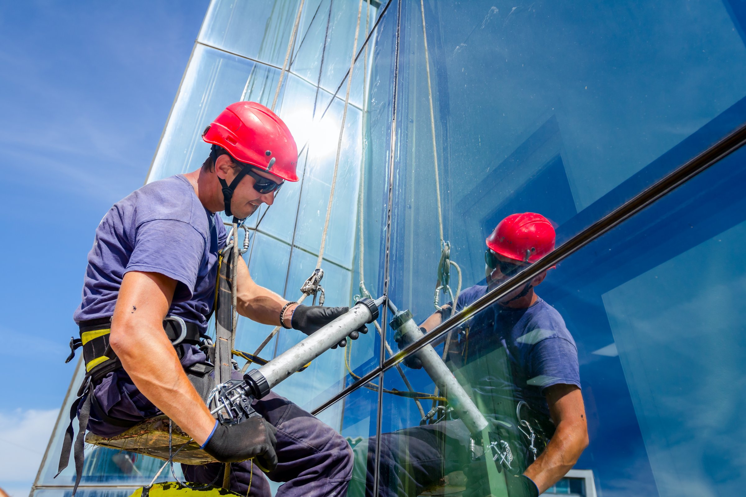 Industrial climber is applying silicone to rubber juncture among building glass facade.