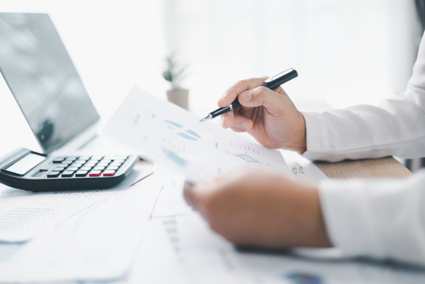 A businesswoman reviews financial report while holding documents and pointing with pen at office desk. Concept of accounting, budget management, financial analysis and corporate business planning.