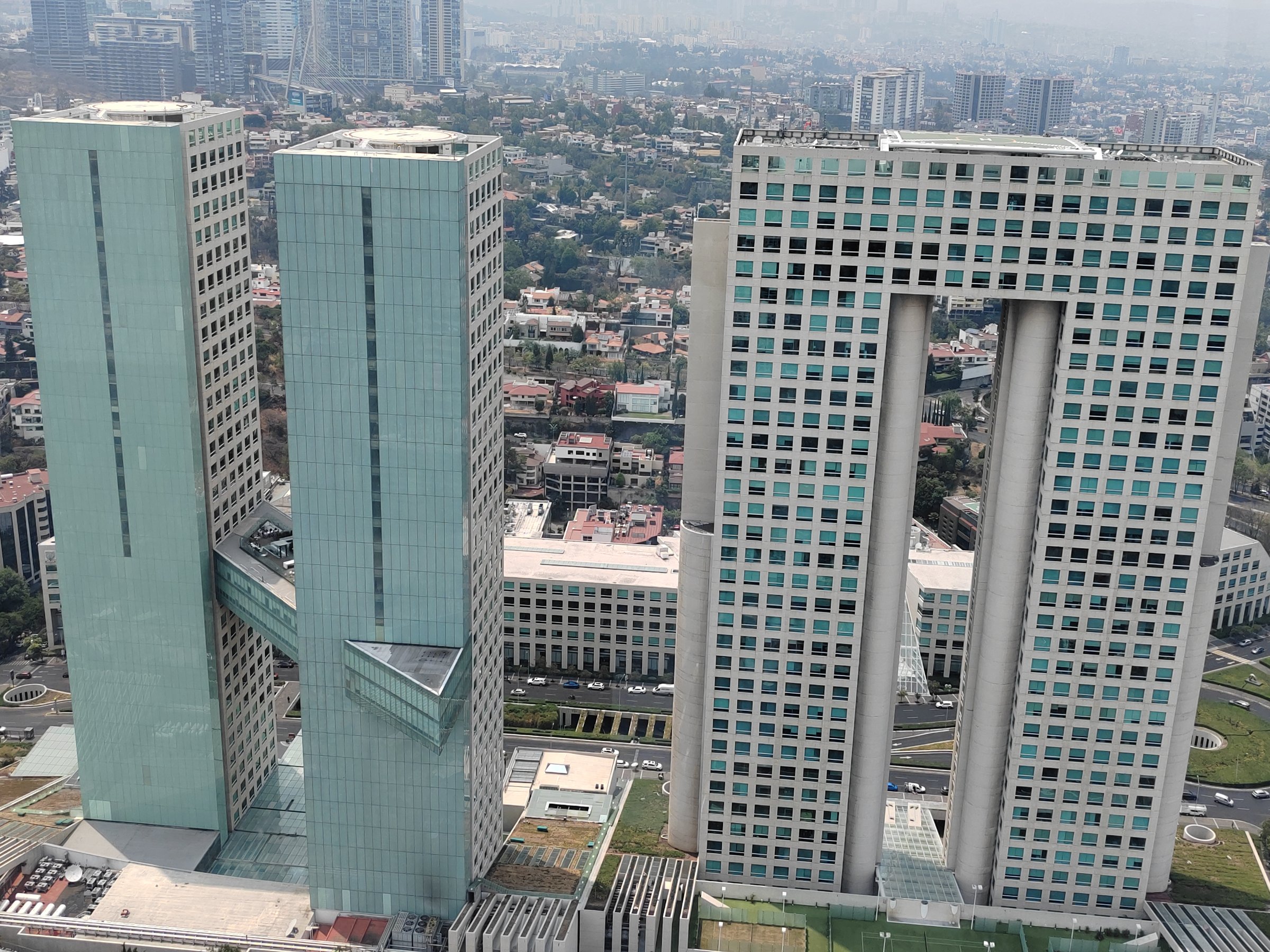 Aerial view of two modern, interconnected skyscrapers with unique geometric designs in a cityscape with cloudy sky.