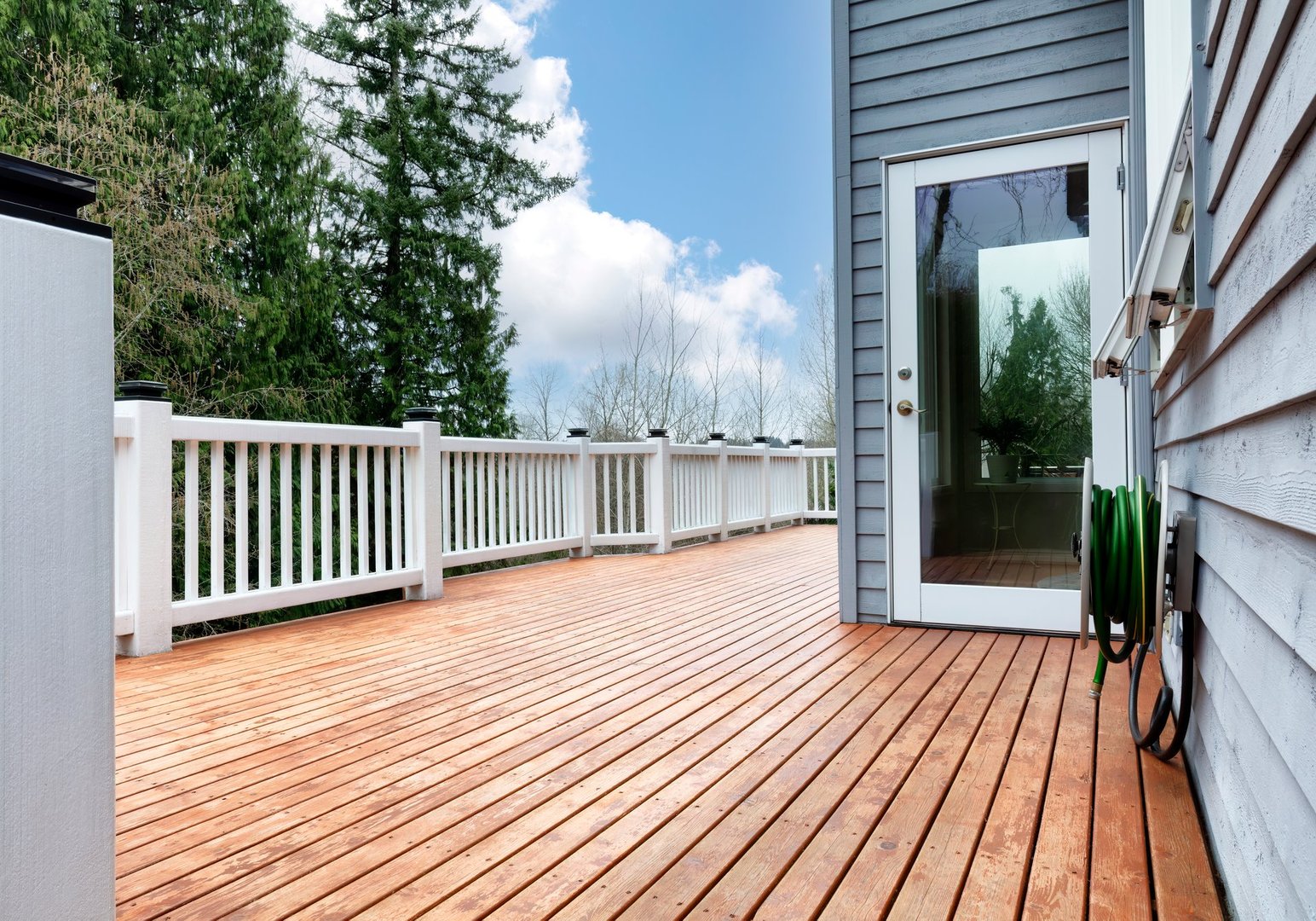 Freshly stain large home walk out cedar wood deck patio with trees and sky in background