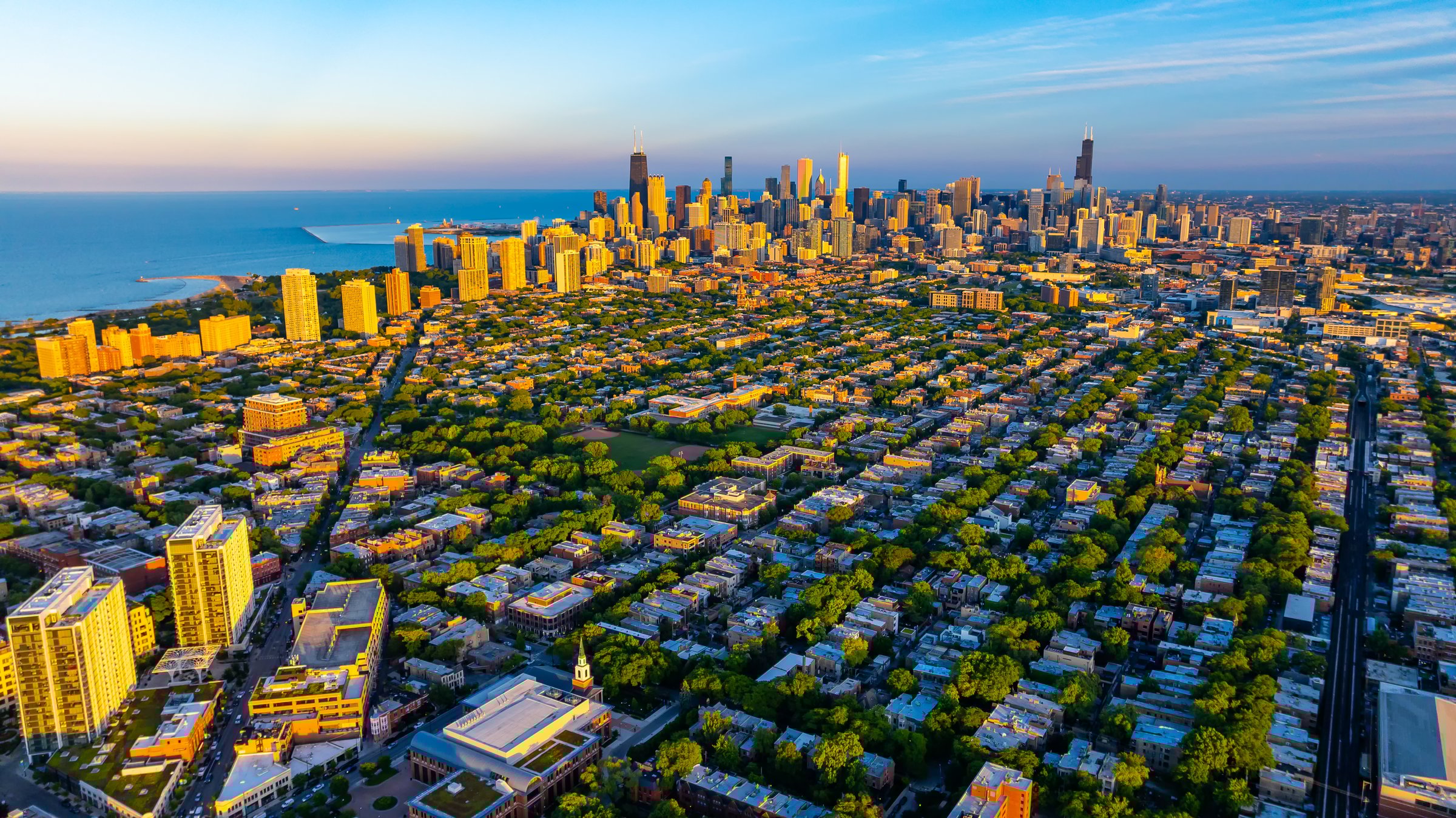 Green uptown and high-rise downtown of Chicago, Illinois in the rays of setting sun. Amazing blue waterscape of Lake Michigan at backdrop.