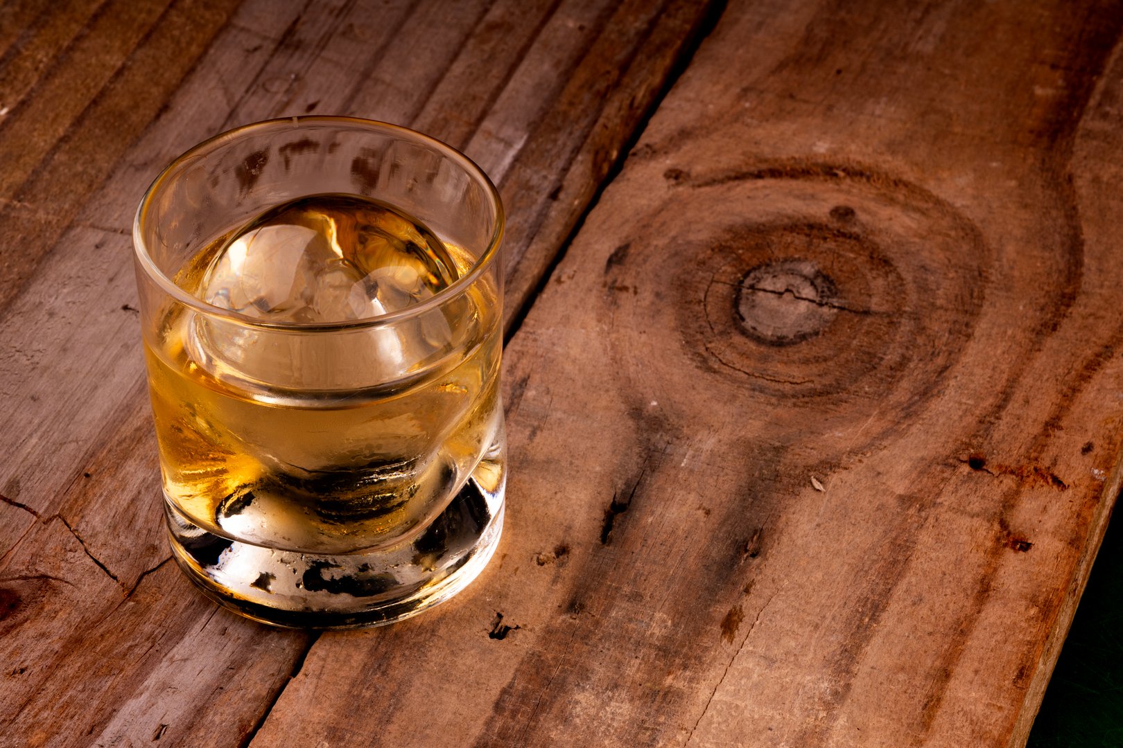 single malt whiskey in specific glass with clear ice in sphere isolated on rustic wooden table