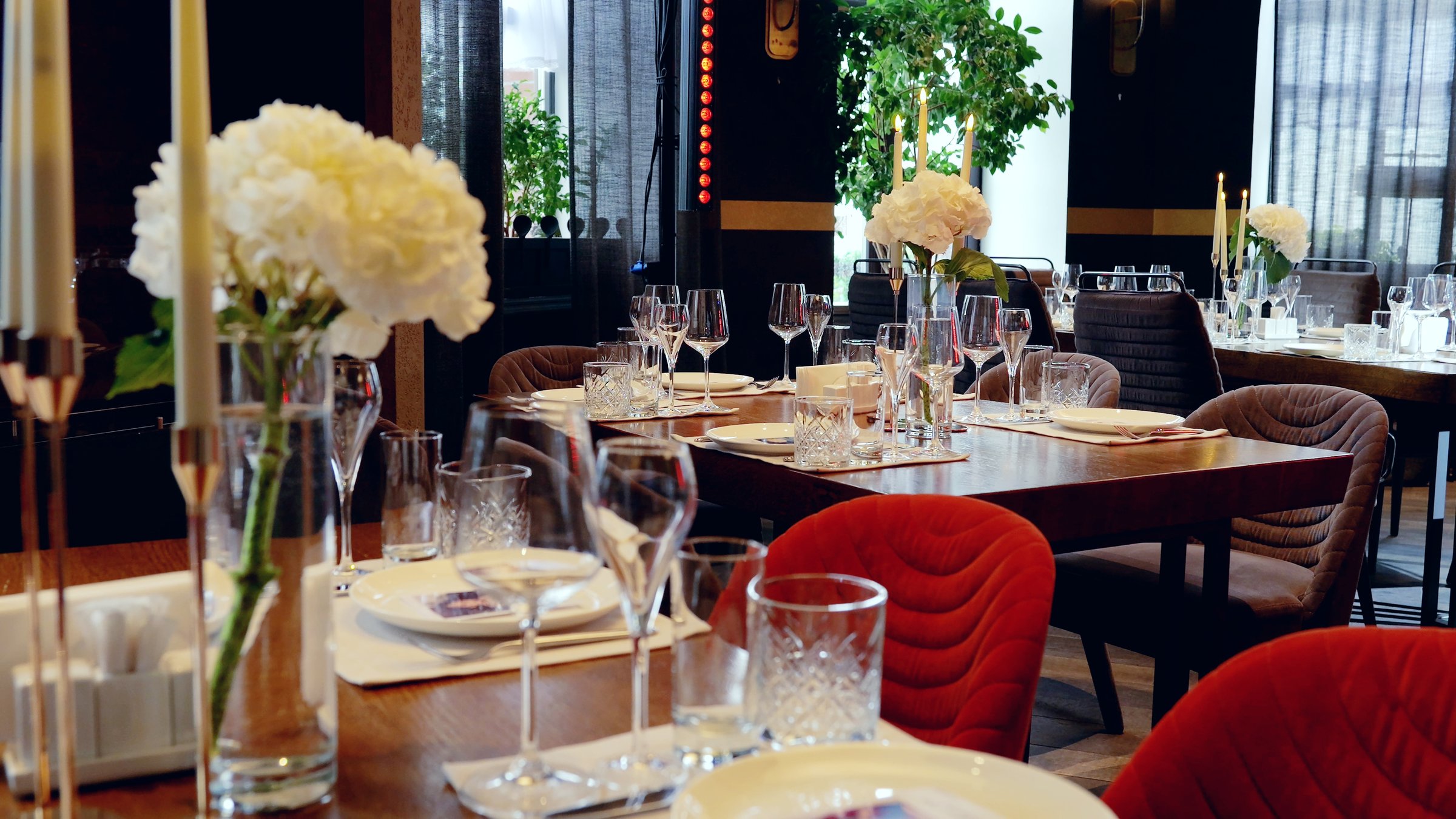 Pristine table setting featuring polished wooden surfaces, crisp white plates, sparkling crystal stemware, silverware, delicate floral arrangements, and elegant tall candles in upscale dining venue