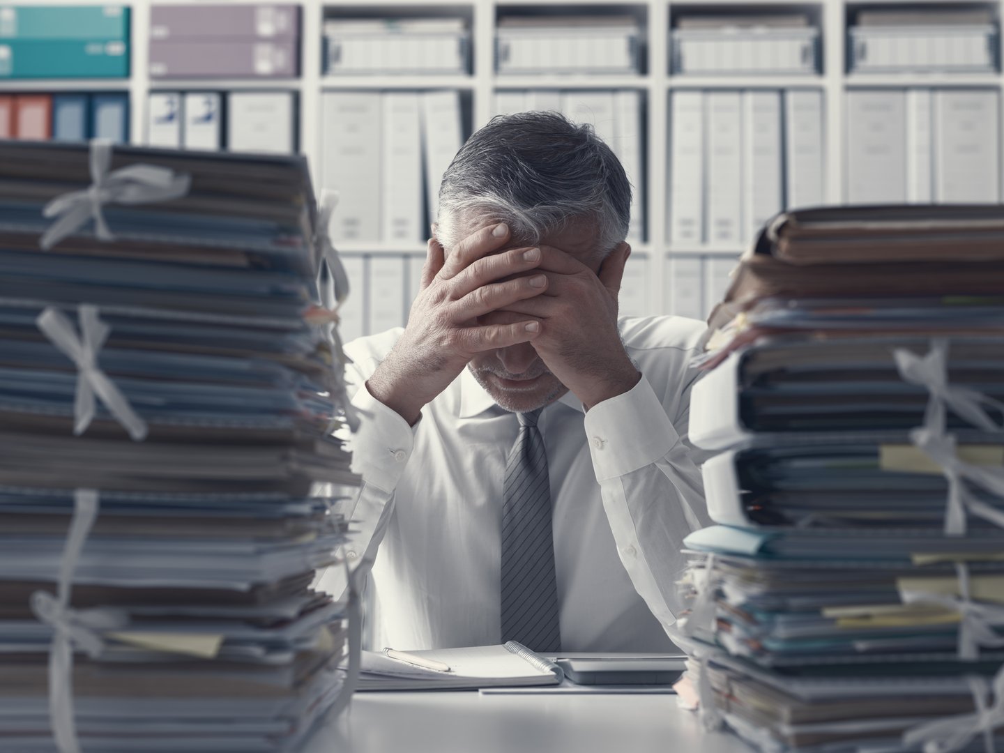 Stressed exhausted business executive in the office overloaded with work, he has stacks of paperwork on the desk