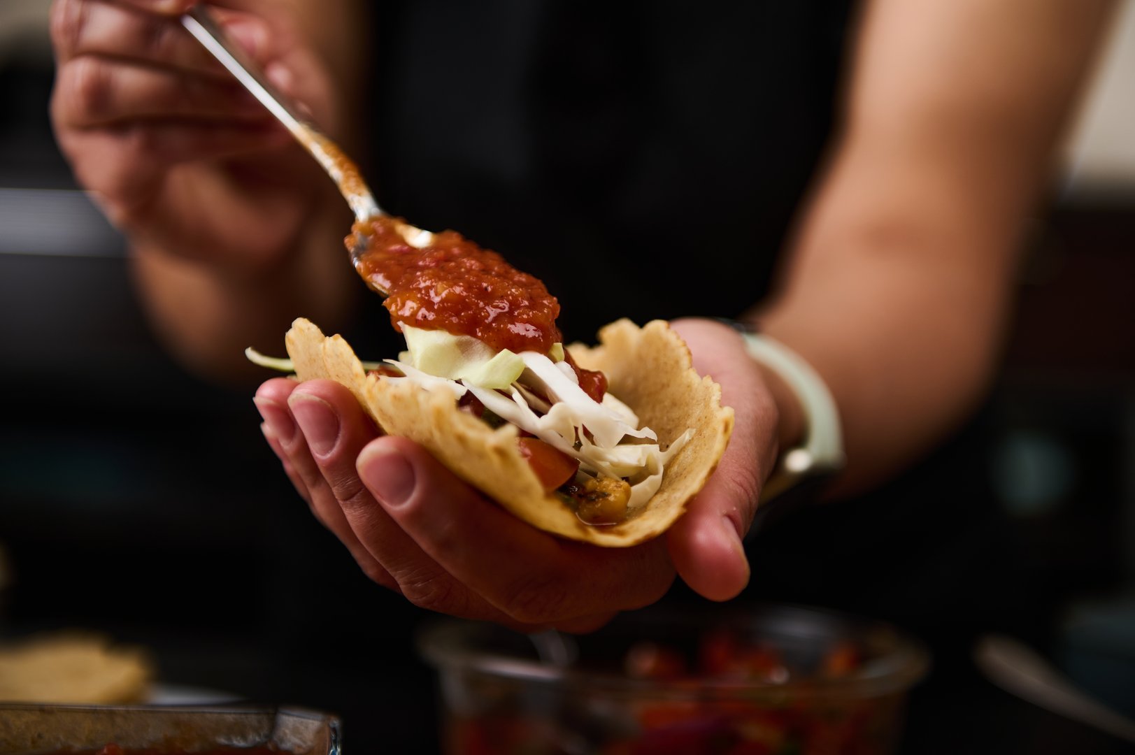 A person assembles tacos filled with fresh vegetables and vibrant salsa, showcasing delicious homemade cooking.