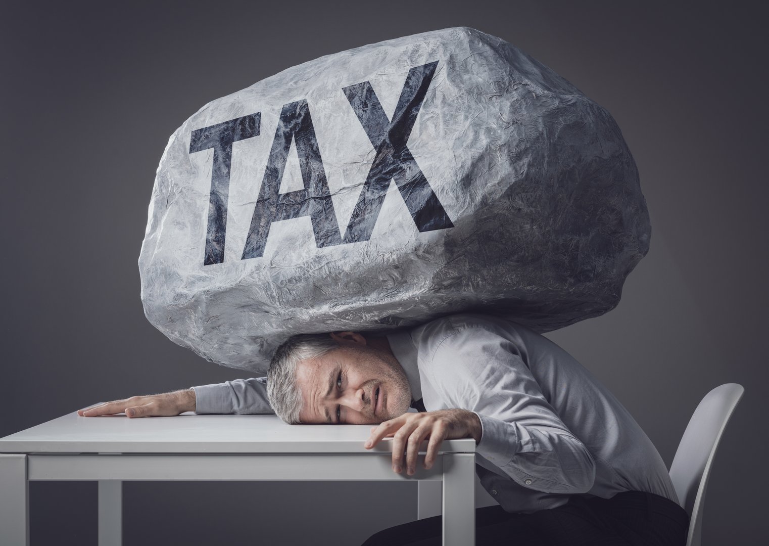 A businessman sits at his desk with a massive boulder marked 