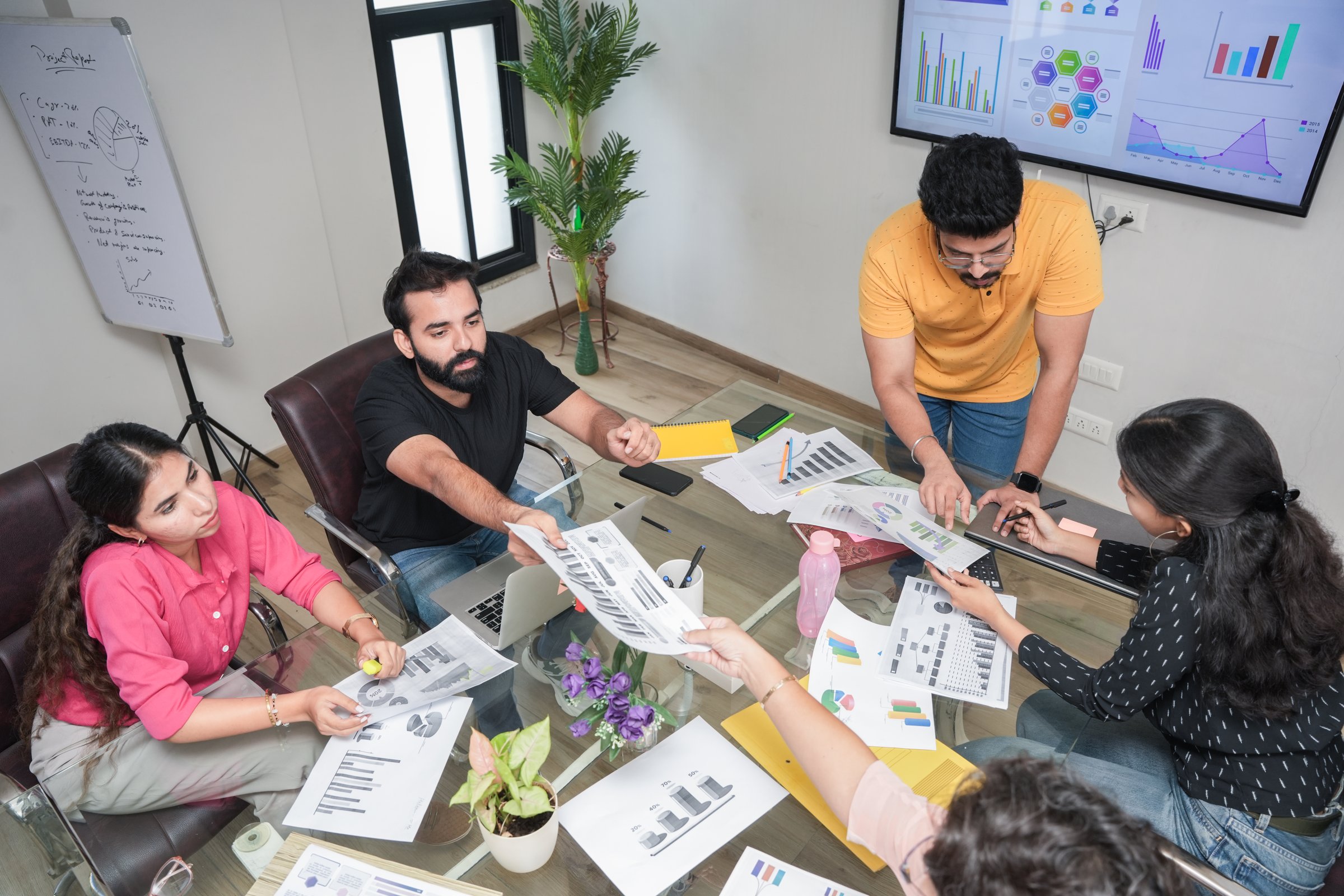 Young indian man discussing planning strategy for business growth with colleagues in meeting room with financial charts and diagram. analysis, sales-up culture. Teamwork, Marketing.  Top angle