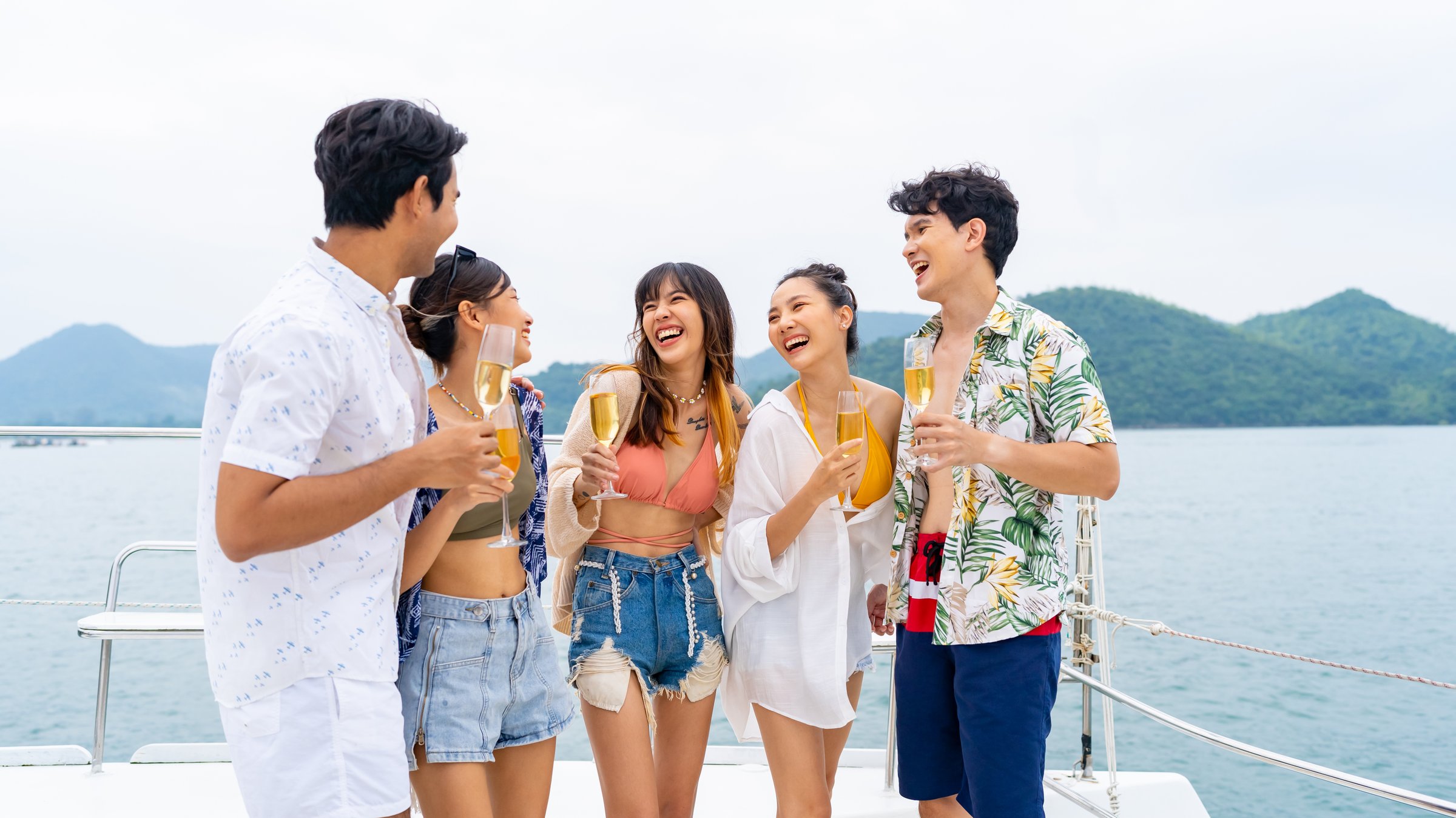 Group of Asian man and woman friends enjoy and fun luxury outdoor lifestyle celebration party drinking champagne together while travel on catamaran boat yacht sailing in the ocean on summer vacation