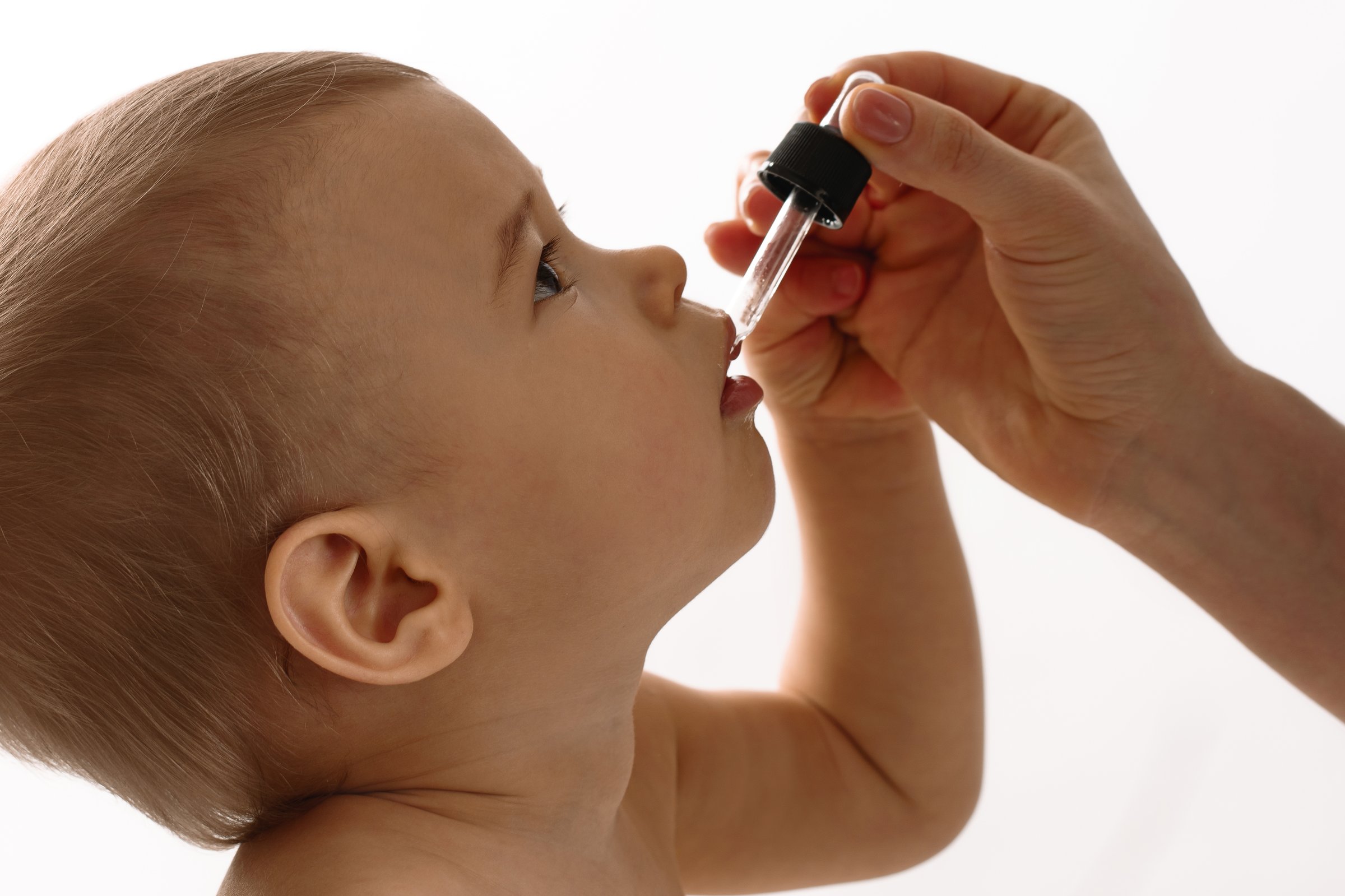 Mother uses pipette to give her little son vitamin D on white background.