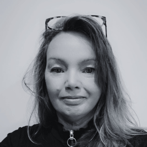 Woman with shoulder-length blonde hair wearing a dark top against a blurred background.