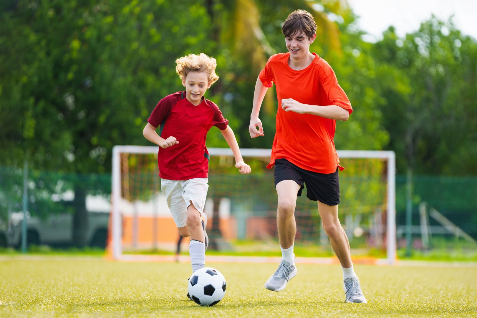 Child playing football. Kids play soccer on outdoor pitch. Little boy kicking ball in summer park. Healthy activity for young children. School sport club team. Football junior league.