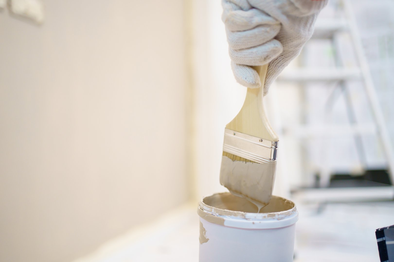 Happy Asian young woman using painting brush painting the empty white wall at inside her house, Home renovation and DIY concept. Cheerful woman enjoy paints the wall by using painting brush.