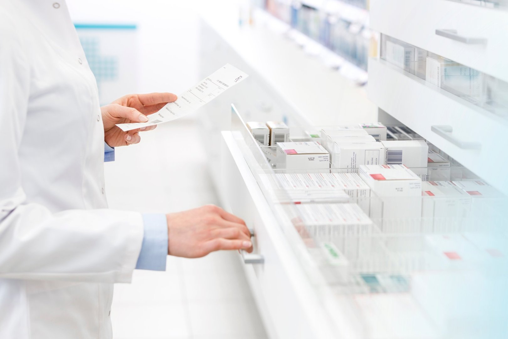 Pharmacist holding a prescription, organizing medication boxes in a pharmacy drawer.